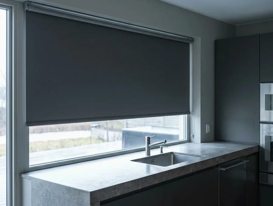 A single smooth blockout roller blind on its tube over a wide kitchen window — one flat sheet, no folds